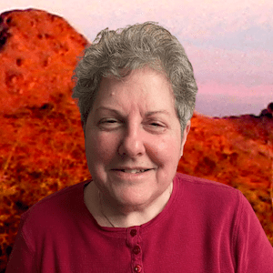The background has a hazy pink, blue, and white sky with red mountains, and then a white woman in front of them. The woman is seen from the top of her head to her shoulders. She has short, curly, and gray/white hair with squinting eyes and a small smirk that shows a few front teeth. She is wearing a red long sleeve button down shirt.